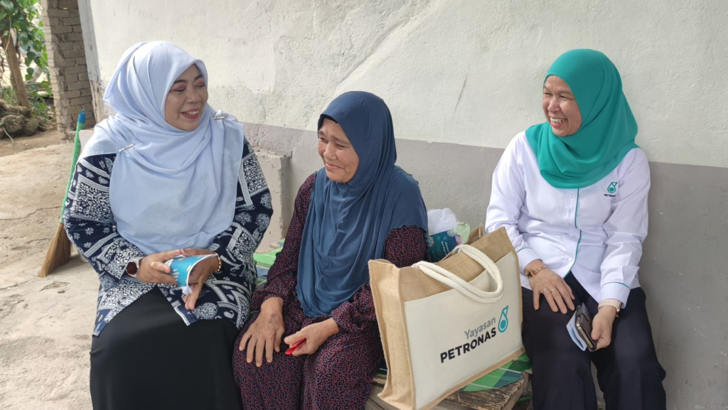 Dato’ Hajjah Halimaton Saadiah, Kedah State Executive Councillor, Chairman of the Women, Family, Community and Welfare Development Committee (left) and Shariah Nelly Francis, Chief Executive Officer of Yayasan PETRONAS (right) handing over a food pack to a beneficiary at her home in Sik, Kedah, as part of the Memacu Kehidupan: Hari Raya Aidilfitri 2023 Programme, which will continue to other districts and regions in the coming weeks.